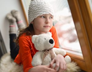 Adolescent girl holding teddy bear looks out window