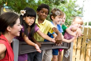 Group of children blow bubbles over bridge while adult woman supervises