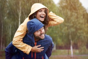 Smiling man carries laughing woman on his back through rain