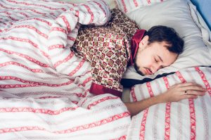 Man sleeping under striped comforter in silk pajamas