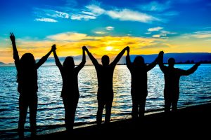 Group of people on beach at sunset raising linked hands to sky