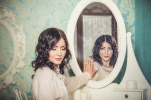 Woman looks away from mirror, downcast, while her reflection smiles
