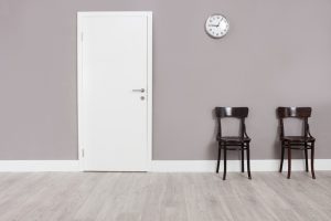 Two wooden chairs in a waiting room with a clock hanging on the wall above them