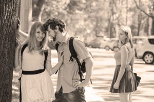 Young woman looks back at laughing, happy couple with distressed and envious expression