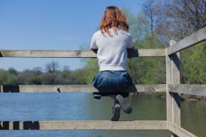 Rear view of woman sitting on fence overlooking lake