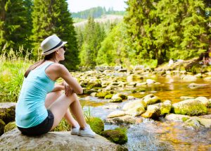 Woman in athletic clothes sits on rock and looks out at pond