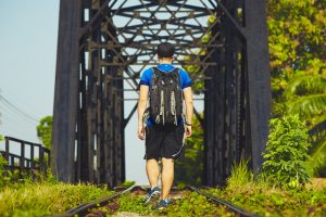 Rear view of backpacking traveler walking along train tracks under bridge