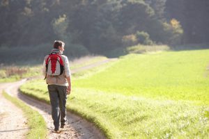 Young man walks along path through grassy hill