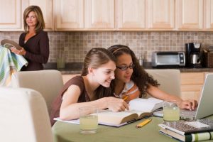 A woman dries dishes while teen friends talk