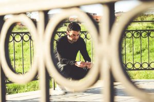 Person in black sits against fence with sad expression