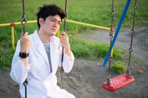 Person in white lab coat sits on swing looking thoughtful