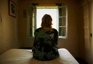 Person seated on bed looks out open window