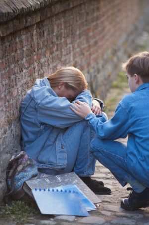Young teen pats arm of other teen who is hiding face
