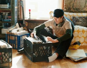A young adult sits in apartment looking through box of records