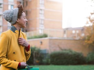 Young person in yellow coat smiling on college campus