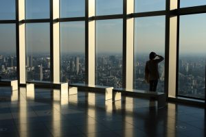 Person looks out over city from windowed room in skyscraper.