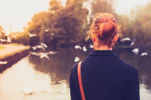 Rear view of red-haired person in black coat watching birds at a lake