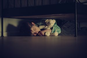 A scared child has fallen asleep under a bed with a teddy bear