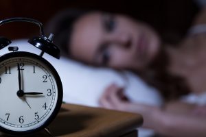 Close-up of alarm clock on night table, blurred person in bed awake