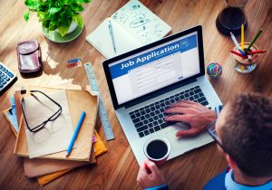 Adult sitting at table uses computer to apply for job