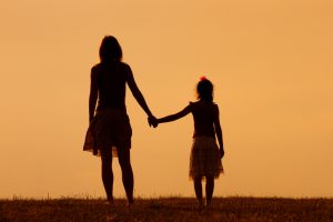 Rear view of mother and daughter hold hands at sunset