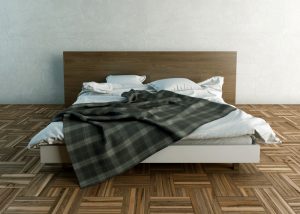 An empty, unmade bed with a plaid blanket in the middle of a room