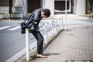 A young professional hides face in hands while leaning against a fence