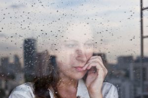 Sad woman looking out rainy window at city