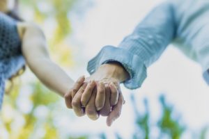 Close-up shot of couple holding hands. Blurred focus on sky and trees in background.