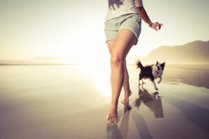 Torso and legs of teenager running along beach with dog