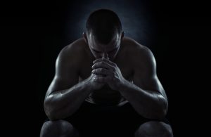 Young athlete on black background with face pressed to interlocked fingers