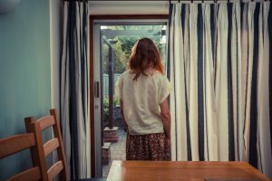 Rear view of person standing by curtains of French doors and looking out