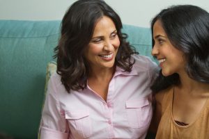 mother and teenage daughter sit and talk on sofa