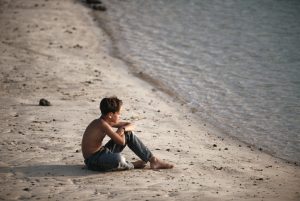 Elevated view of young boy sitting on a beach staring out at sea