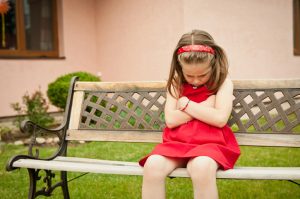 Young child sits on a bench looking down, arms crossed over chest