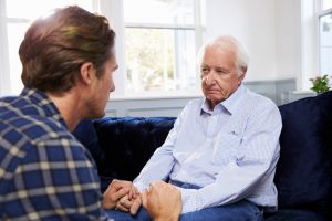 Adult son holds father's hands while the two talk