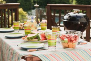 Fresh fruit, lemonade, place settings, and barbecue grill spread across picnic table