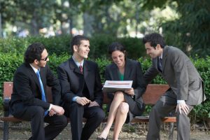 Four people in business dress with open, cheerful faces sit on park bench