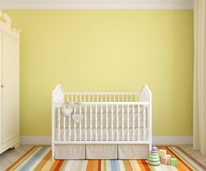 A white crib sits in a bright nursery with yellow walls and striped rainbow rug