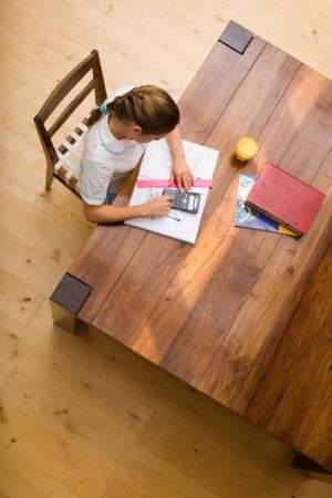 Overhead view of preteen student does homework at kitchen table with school supplies spread around