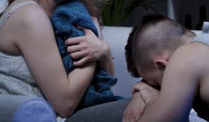 cropped view of person clutching blanket while second person kneels in apologetic stance