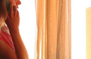 Cropped image of person speaking on phone at curtaind window with soft light in room