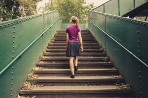 Person in skirt with long ponytail walks up stairs, rear view 