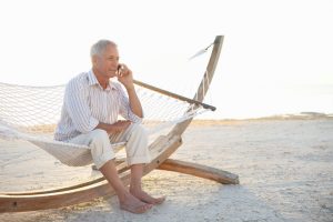 A mature man with gray hair sits on hammock and talks on the phone