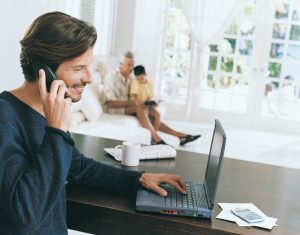 Adult professional works at table while son and older adult sit in background