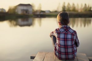 Boy sitting alone on dock overlooking lake