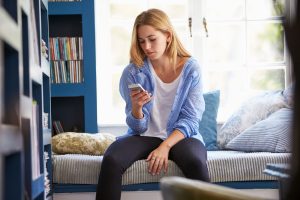 Woman sitting on bed while looking at phone