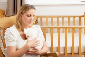 bereaved woman at crib with teddy bear