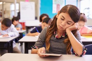 Bored student looks at tablet while sitting at desk in classroom