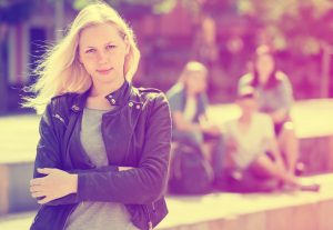 A teenager stands with arms crossed, looking confident, in front of a group of youth in blurred focus